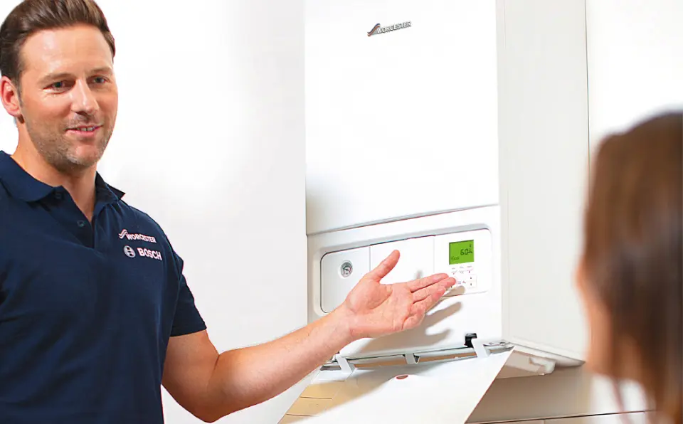 Heating engineer explaining boiler controls to a client in front of a wall-mounted boiler.