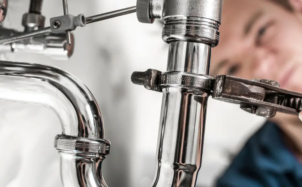 A plumber using a wrench on a chrome pipe fitting in a plumbing installation.