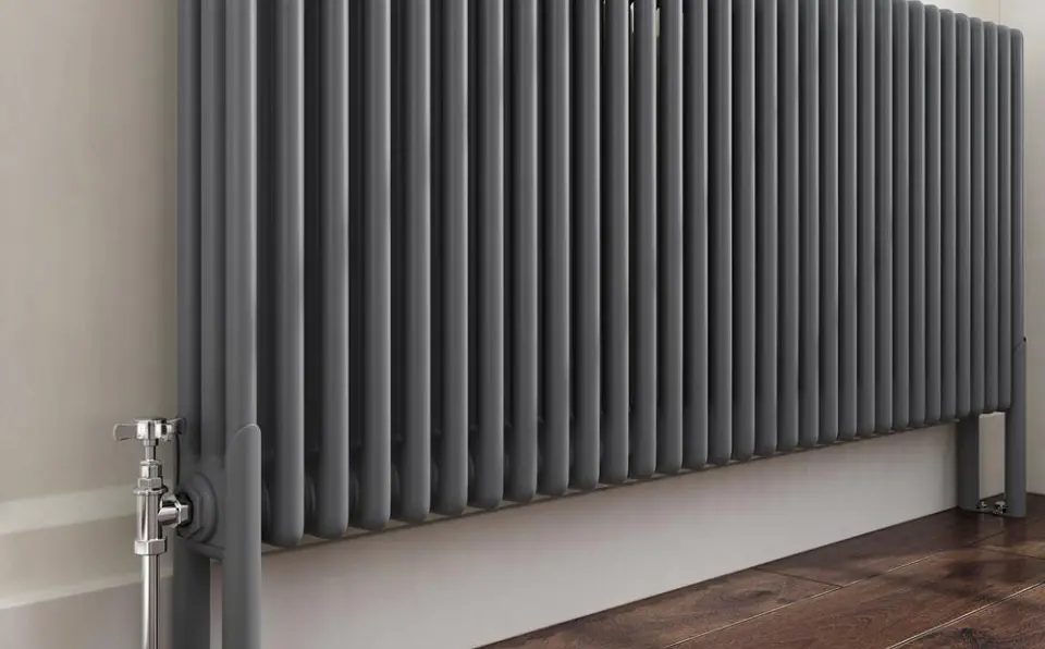 Gray vertical heating radiator with multiple horizontal fins and a valve at the base.