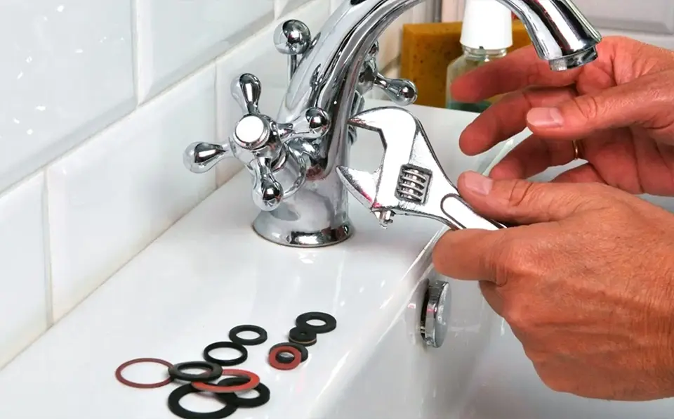 Person using an adjustable wrench to repair a faucet with various washers nearby.