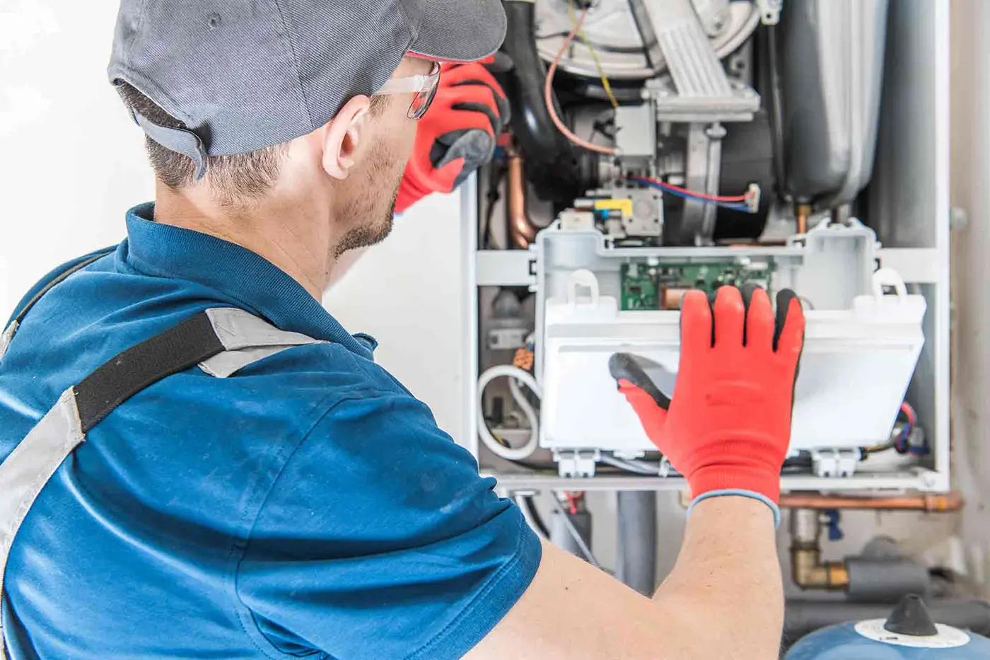 Technician in a blue shirt and red gloves inspecting the internal components of a heating system.
