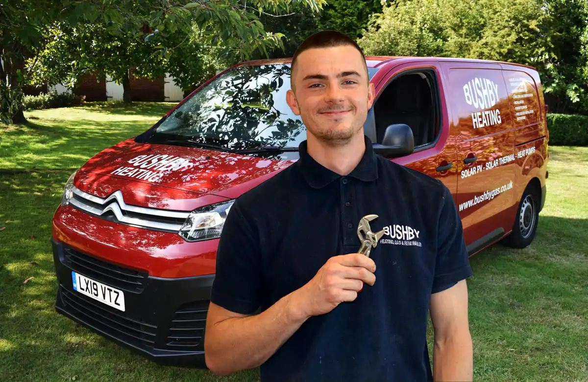 A Bushby Heating engineer holding a wrench in front of a red service van.
